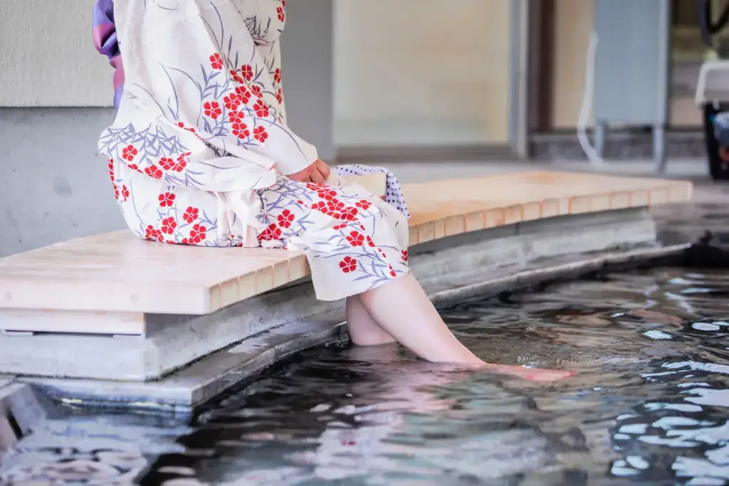 A woman wearing a light summer kimono while dipping her feet in an onsen .