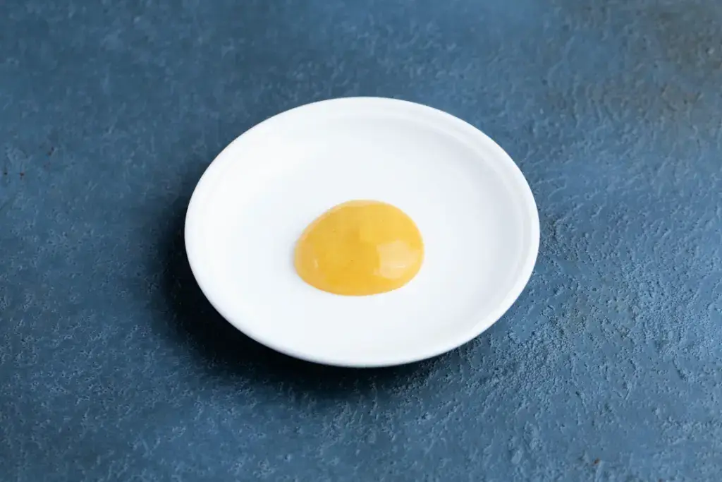 A white plate with a dollop of karashi mustard on a blue background.