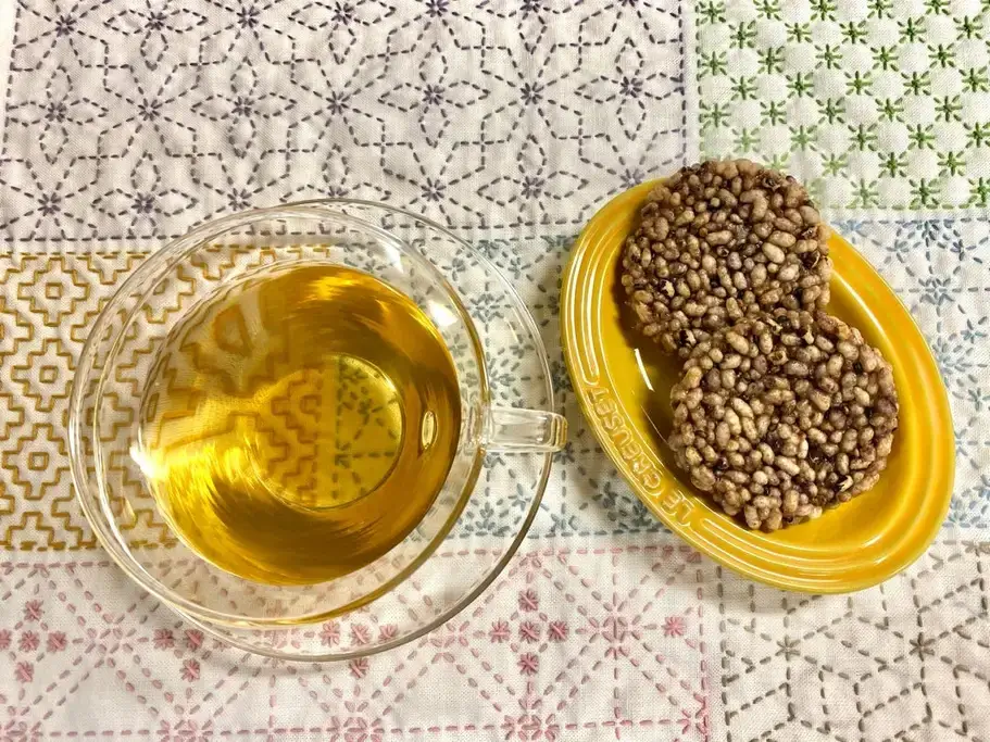 A plate of kodaimai senbei next to a glass of green tea.