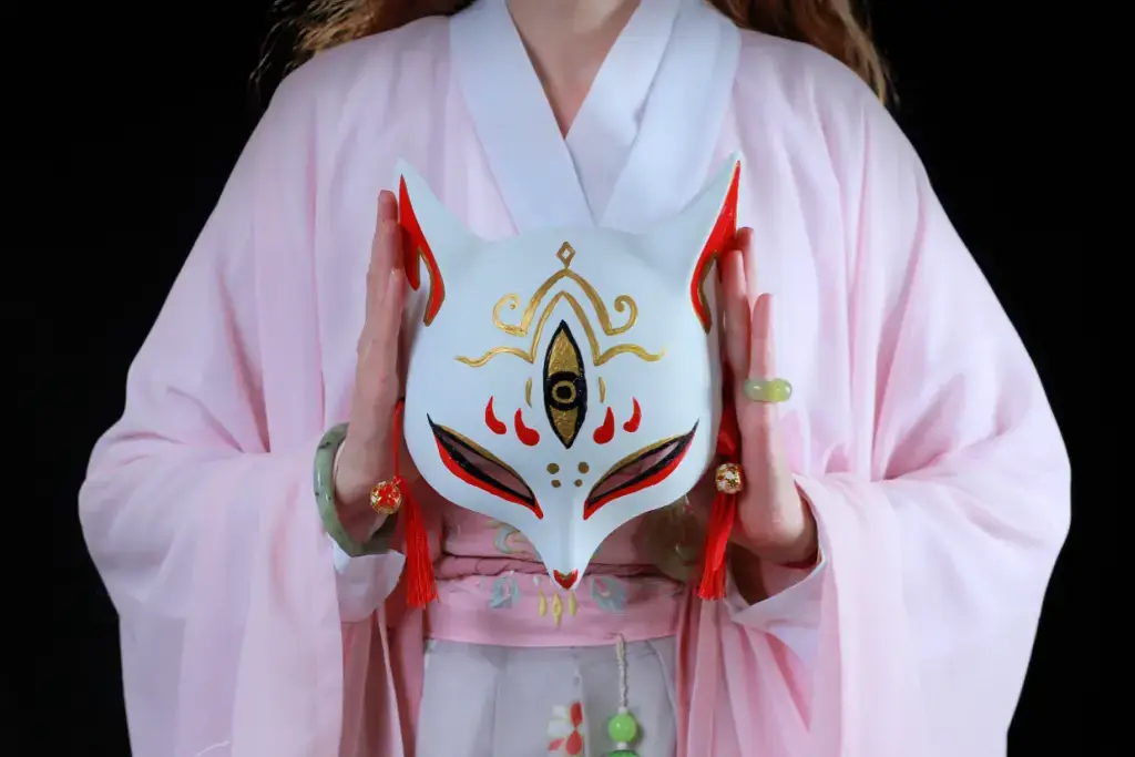 A woman in a pink kimono holding a white kitsune mask.