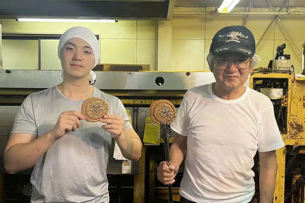 Osamu and Kazue Nakamori from Eisendou in their factory. Osamu is holding up a white sesame senbei.