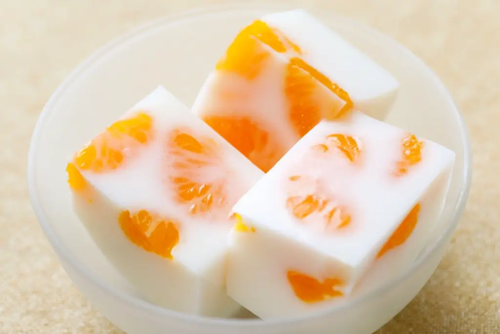 A bowl of milky kanten with orange pieces inside.