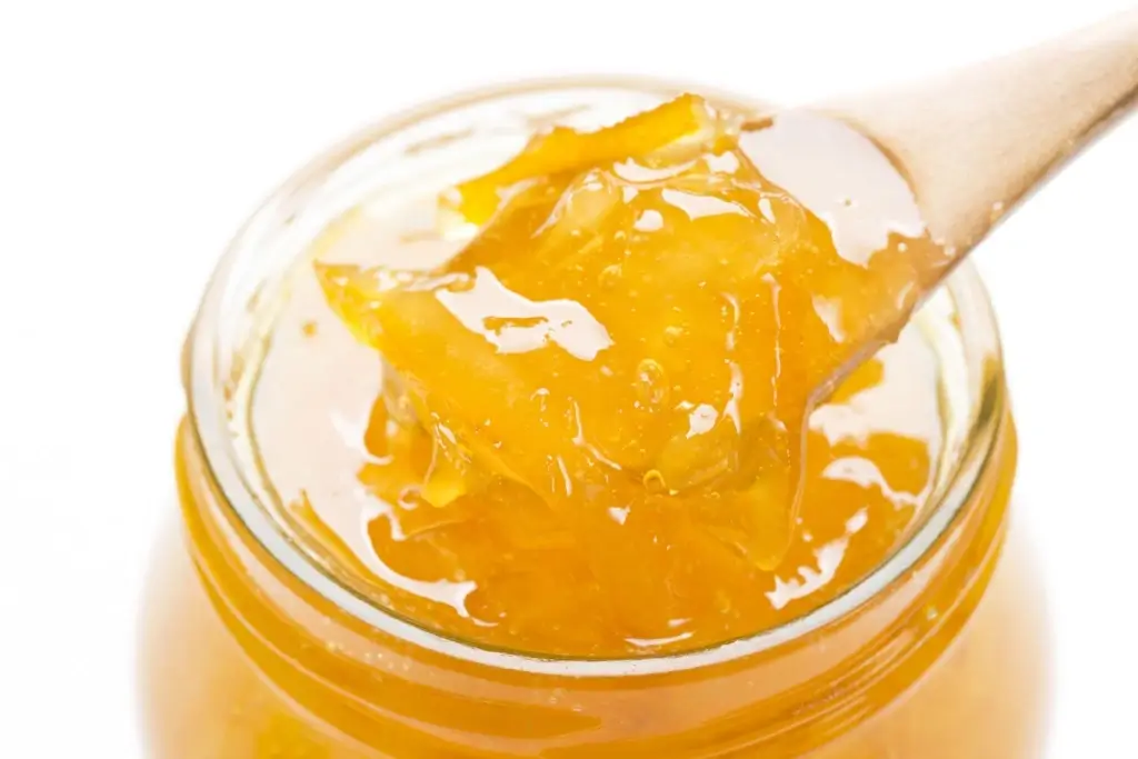 A wooden spoon scoops into a glass jar of yuzu jam.