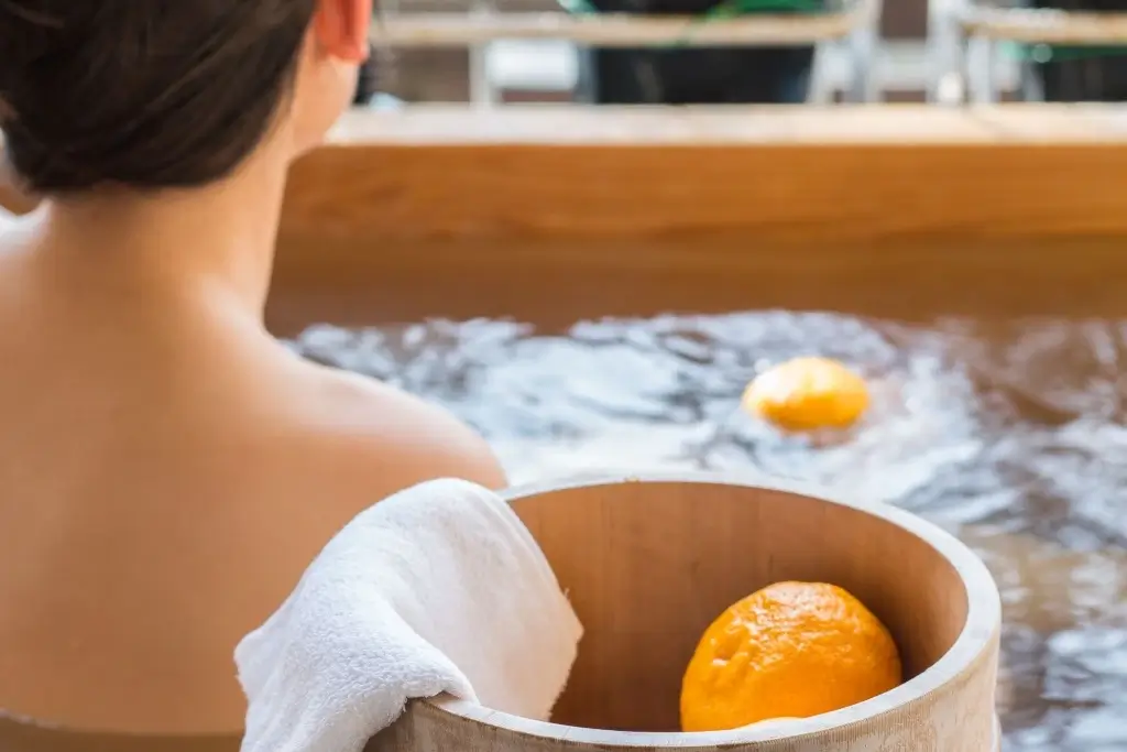 A woman sits in a wooden bathtub with yuzu fruit in Japan.