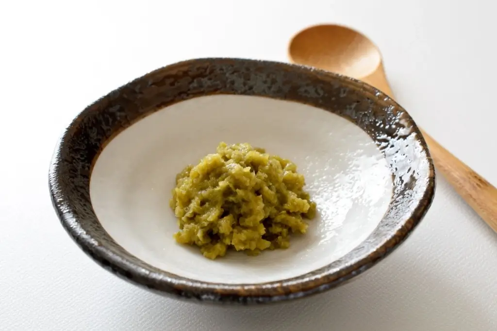 A ceramic bowl displaying yuzu jam sits on a white table.