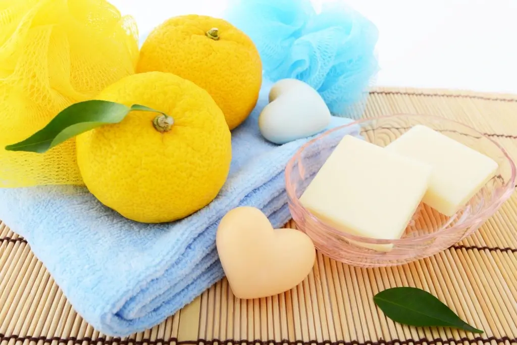 A bunch of yuzu fruit sits next to bath soap on a wooden mat.