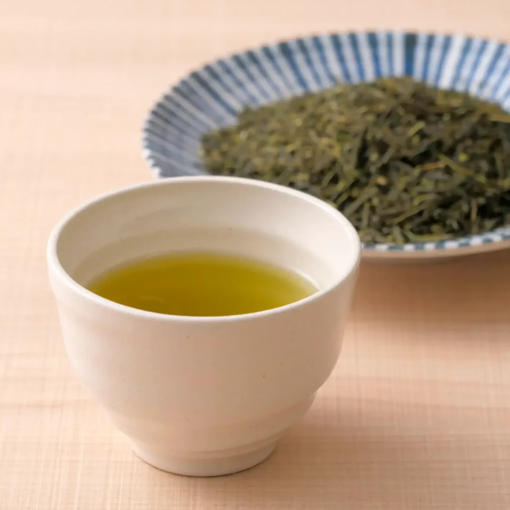 A cup of hojicha with a plate of sencha tea leaves in the back.