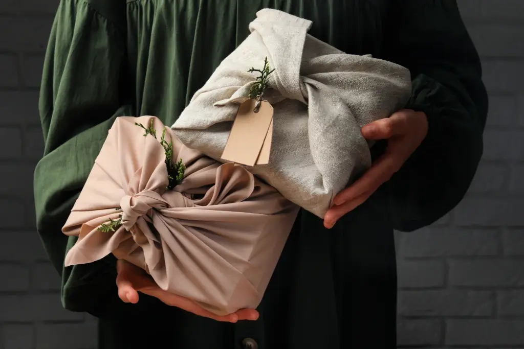 A person handing over authentic Japanese gifts wrapped in brown and grey furoshiki.