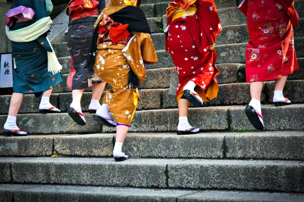 A bunch of women wearing kimonos of red, orange and black as they go up the stairs.