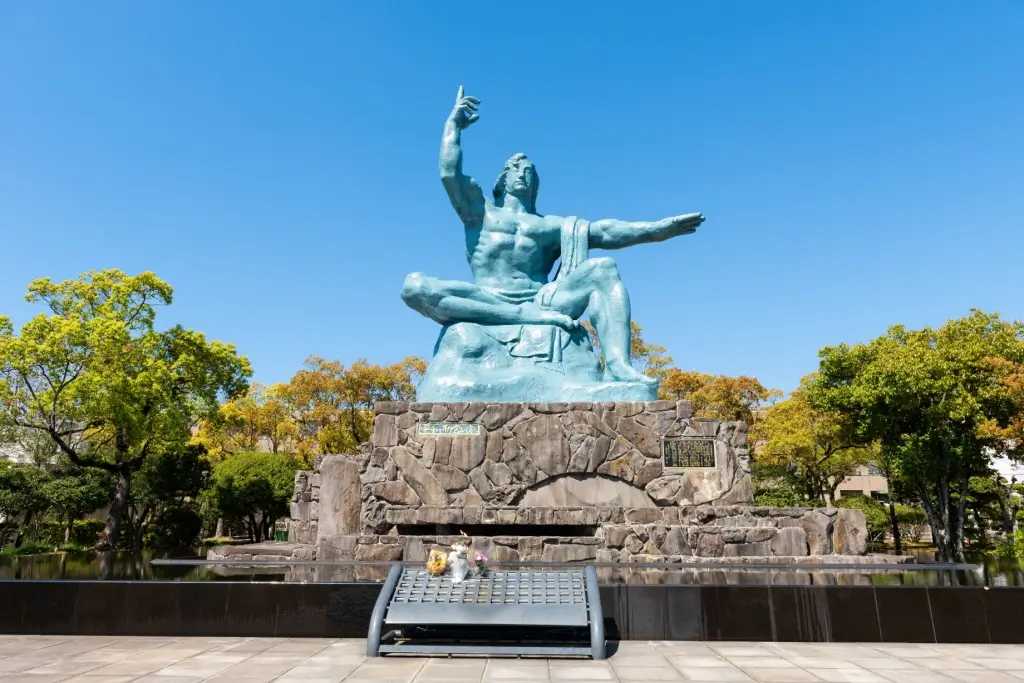 A bronze statue in Nagasaki Peace Park. It's a seated masculine figure, with its right arm pointed up and left hand pointed to the left.