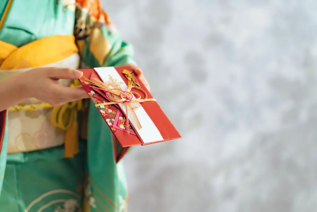 A women wearing a kimono, handing over a red gift gard.