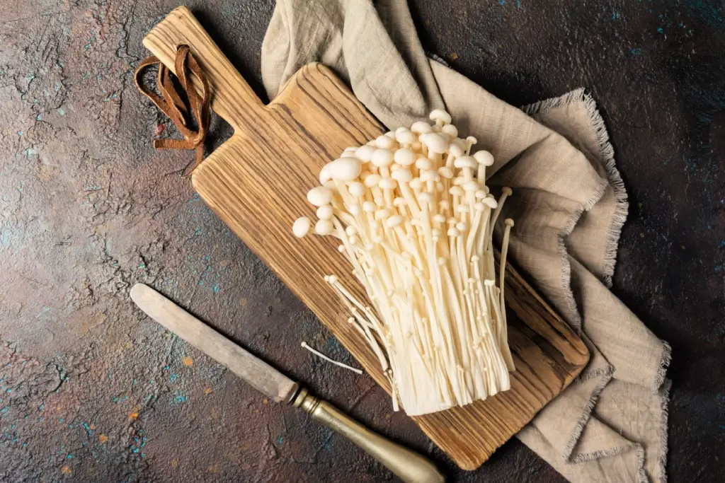 A cluster of enoki mushrooms on a cutting board.