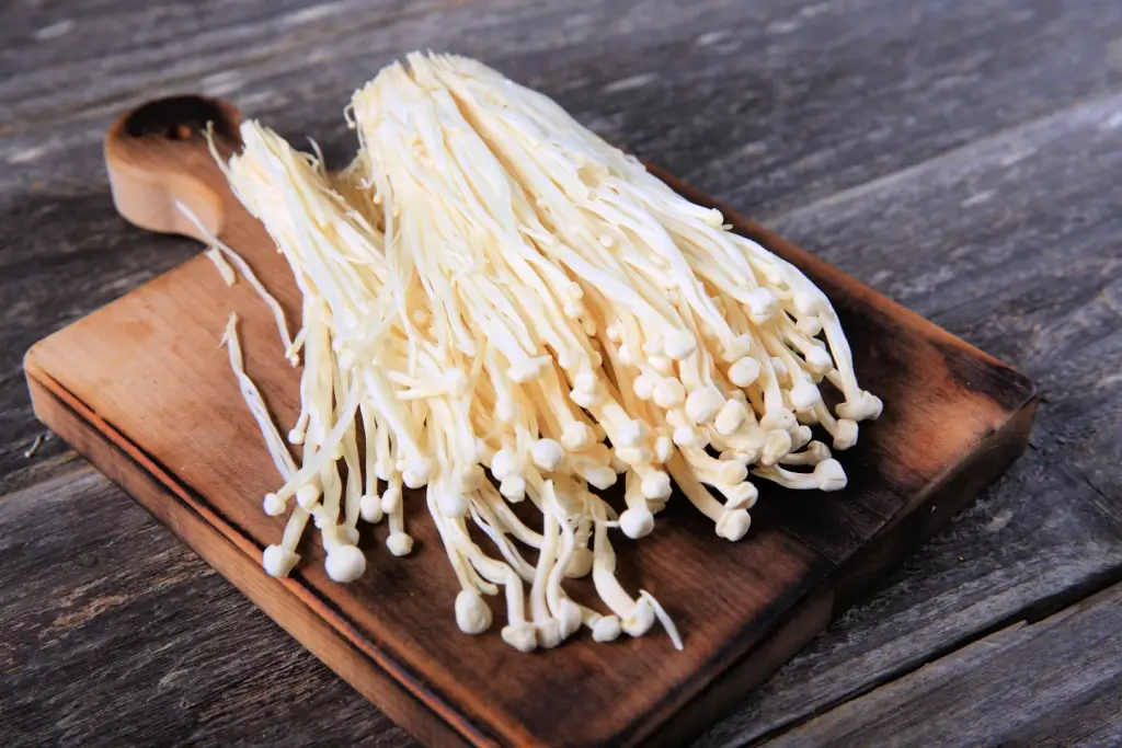 A cluster of enoki mushrooms. They are long and thin, with white heads.