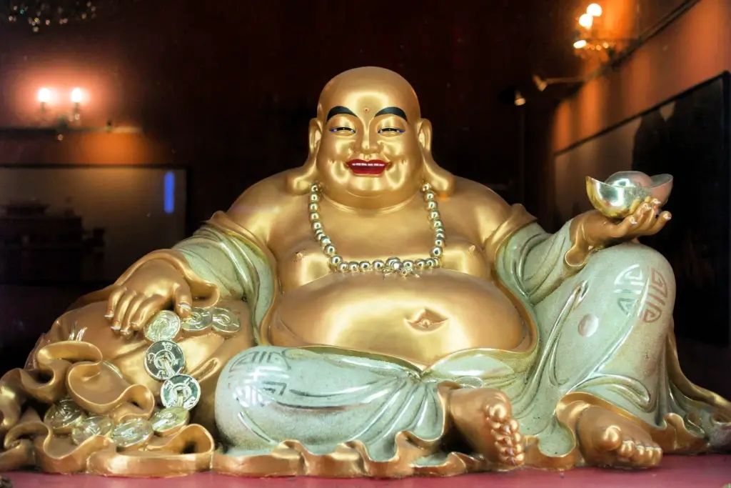 A golden statue of Hotei. He has a bald head and a large belly.