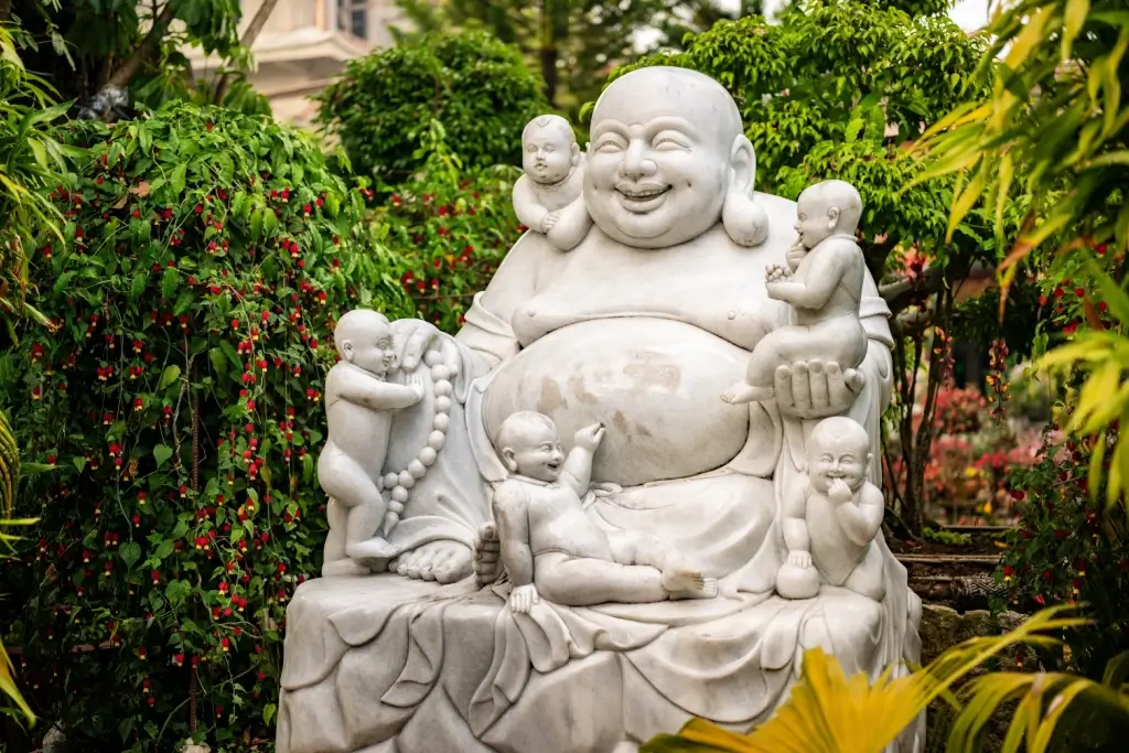 A stone statue of Hotei and children. He has a bald head and large belly.