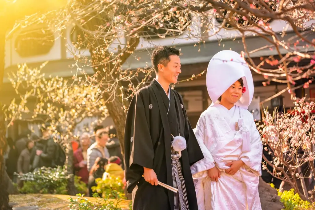 A bridge and a groom at a traditional Japanese wedding. The man is wearing a gray hakama and a black top, and the woman is wearing a white kimono.