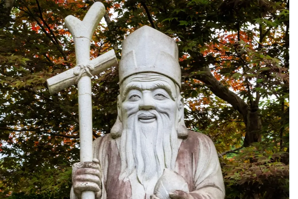 A statue of Jurojin in a park. He looks like an old man with a beard, holding a staff.