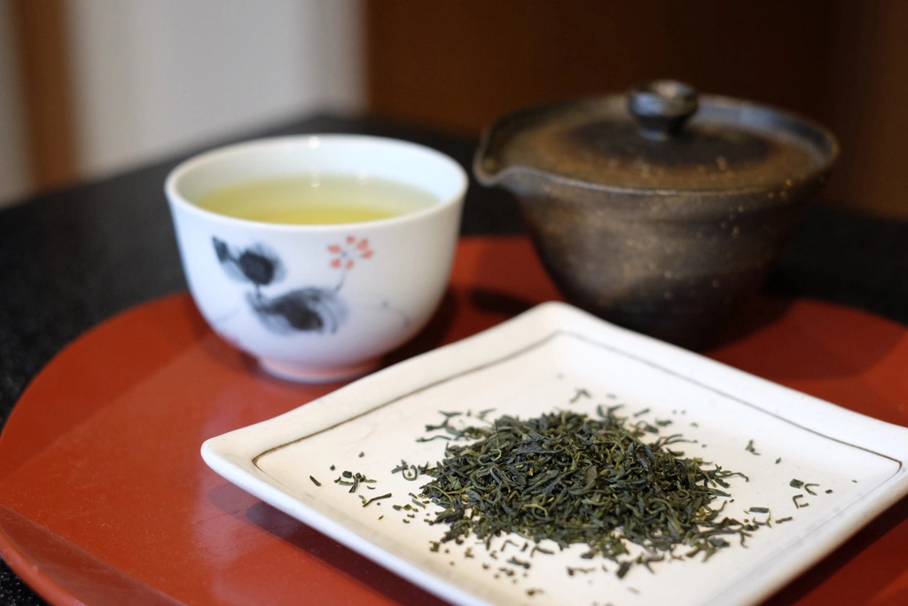 A cup of kamairicha next to a plate of tea leaves.