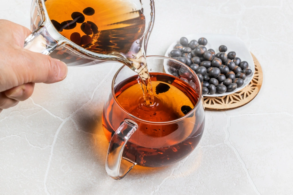 A glass up of kuromamecha, next to a plate of black beans.