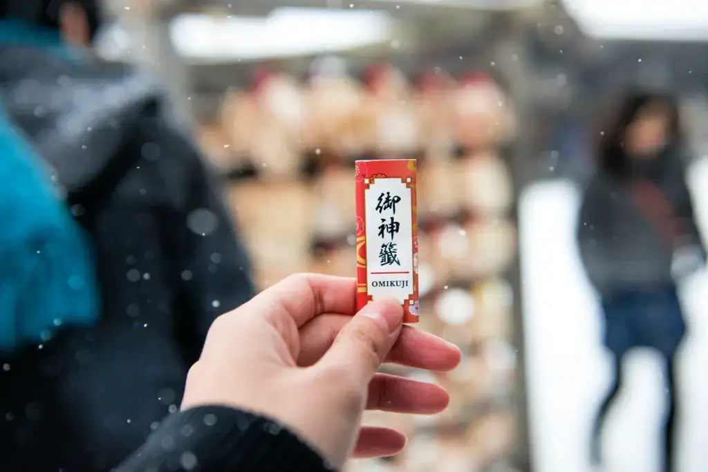 A hand holding an omikuji on a snowy day.