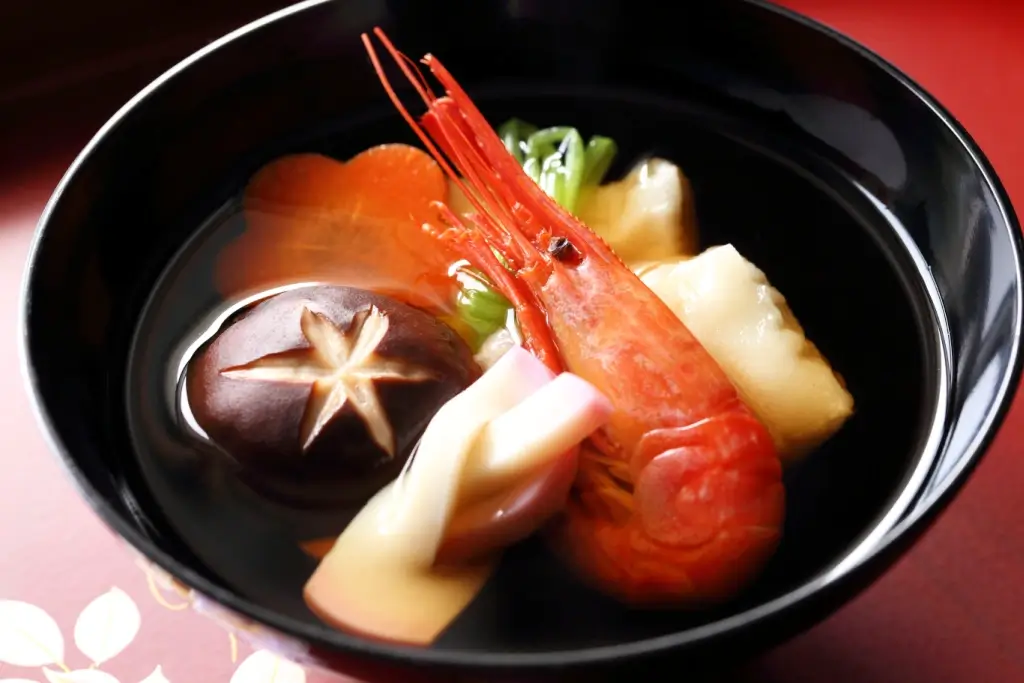 A bowl of clear ozoni soup, with a large shrimp .