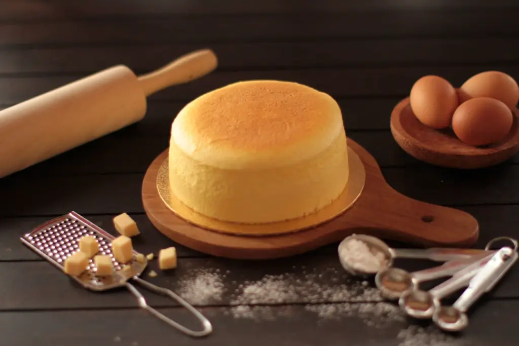 A whole Japanese cheesecake surrounded by its ingredients, eggs, cheese and flour.