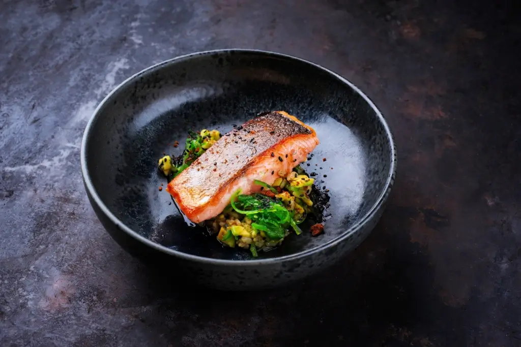 A plate of Japanese fish, salmon on a black plate.