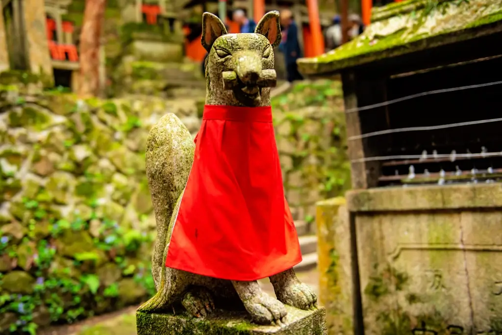 A kitsune statue covered in a red bib.