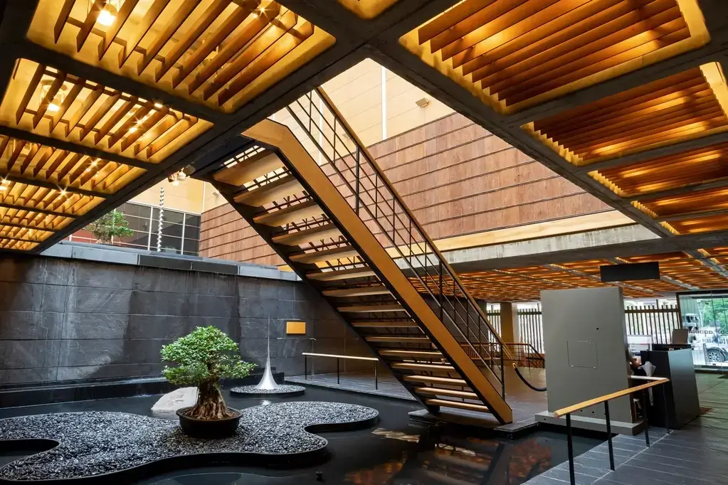 The interior of New York's Japan Society. It has wooden stairs and a bonsai tree,.