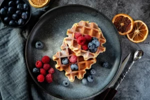 A plate of Belgian waffles with powdered sugar and fruit.