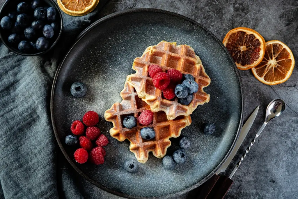 A plate of Belgian waffles with powdered sugar and fruit.