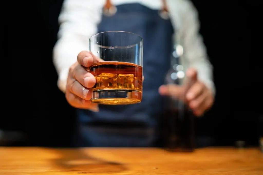 A bartender holding a glass of brown liquor.