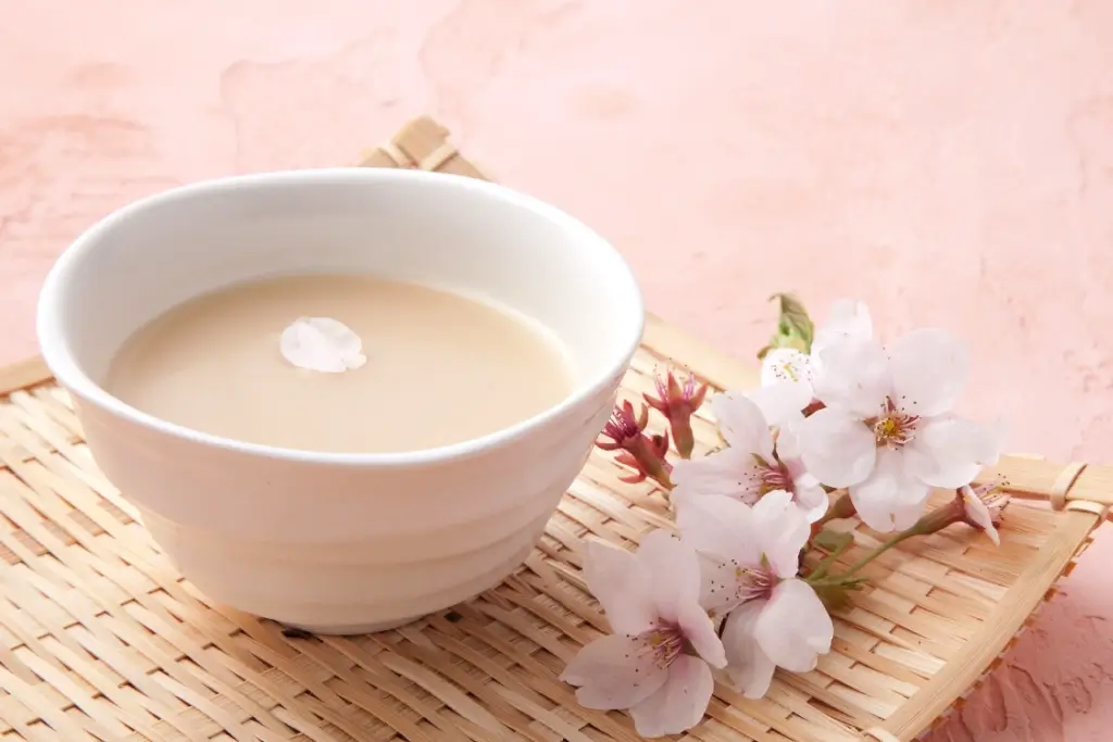 A cup of nigori sake with a cherry blossom petal on its surface.