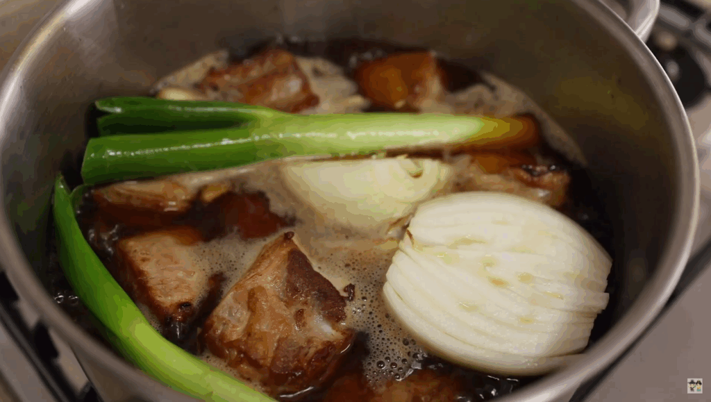 Simmering pork and aromatics in a braising liquid inside a pot